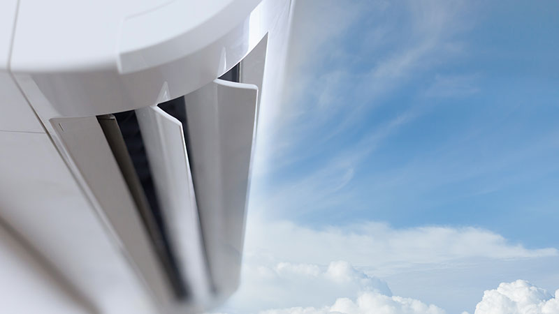 Detalhe de uma unidade interior de um aparelho de ar condicionado, com um céu azul com nuvens como pano de fundo.